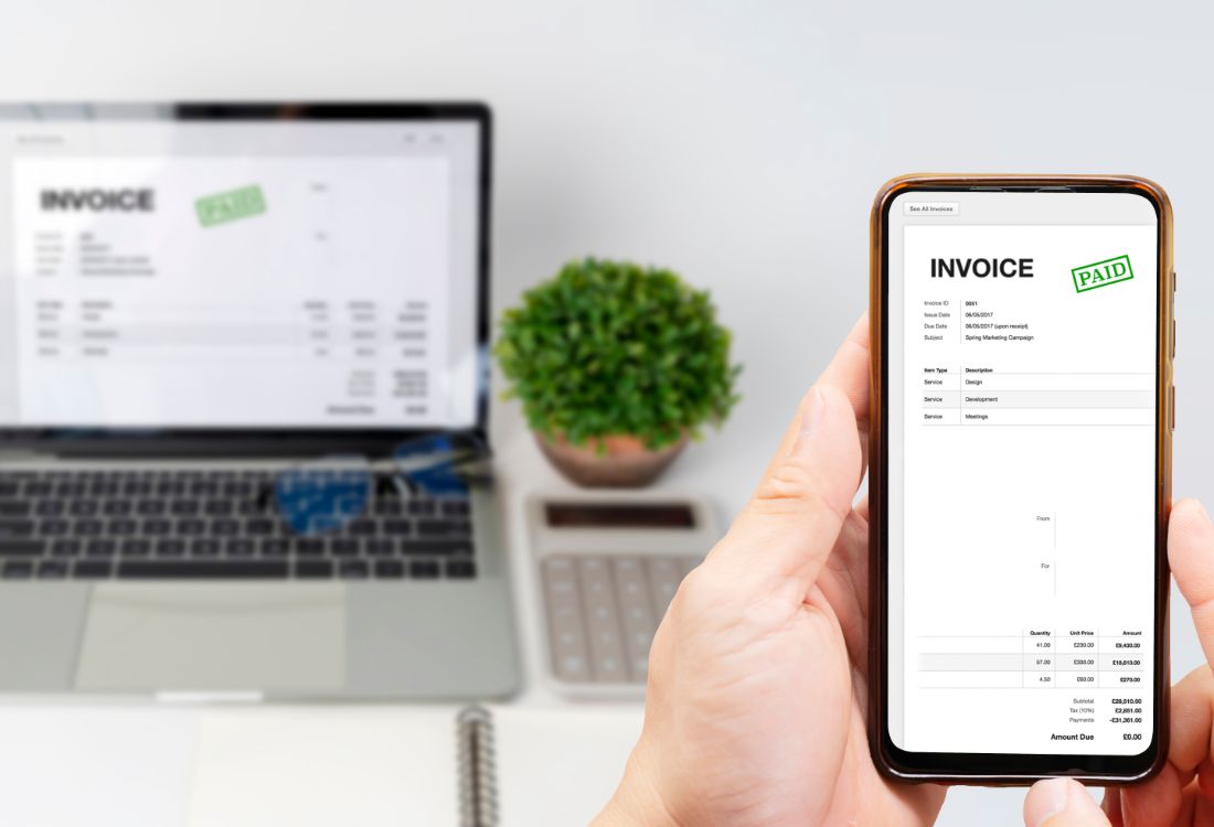 A paid invoice open on a phone, with a laptop showing the same invoice behind it
